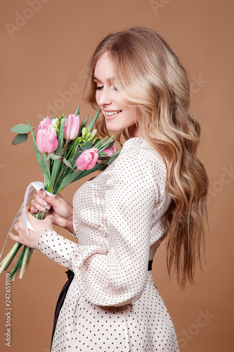 Happy beautiful elegant woman with pink bouquet of tulips over beige background.