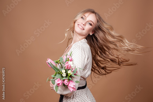Happy beautiful elegant woman with pink bouquet of tulips over beige background. Copy space