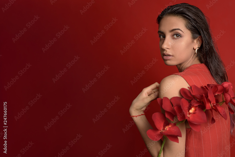Young Woman in a red dress holding a red orchids against red background. Sensual girl back view. Copy space Young Woman in a red dress holding a red orchids against red background. Sensual girl back view. Copy space