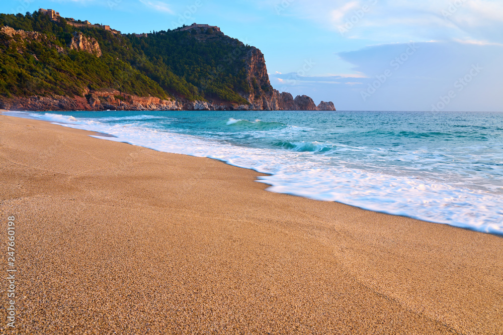 Alanya Castle (Alanya Kalesi) on the top of peninsula. View on sea from sandy Cleopatra Beach, Alanya, Turkey in evening. 