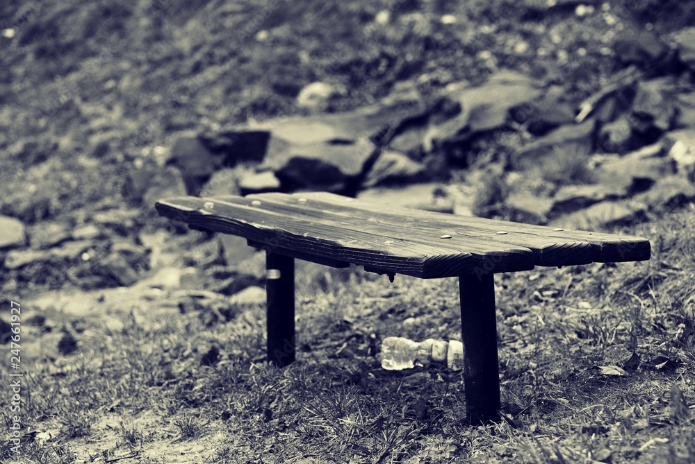 Black and white photo of wood bench, with discarded plastic bottle 