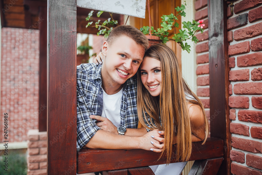 Young family standing at the porch of the house, hugging each other and looking at the camera. Happy smiling couple outside. Young family standing at the porch of the house, hugging each other and looking at the camera. Happy smiling couple outside.