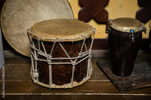 A large drum made of wood and leather,tied with twine. A small drum made of Buffalo leather and mahogany. National musical instruments, on the table, decorative wall background with wooden drawings.