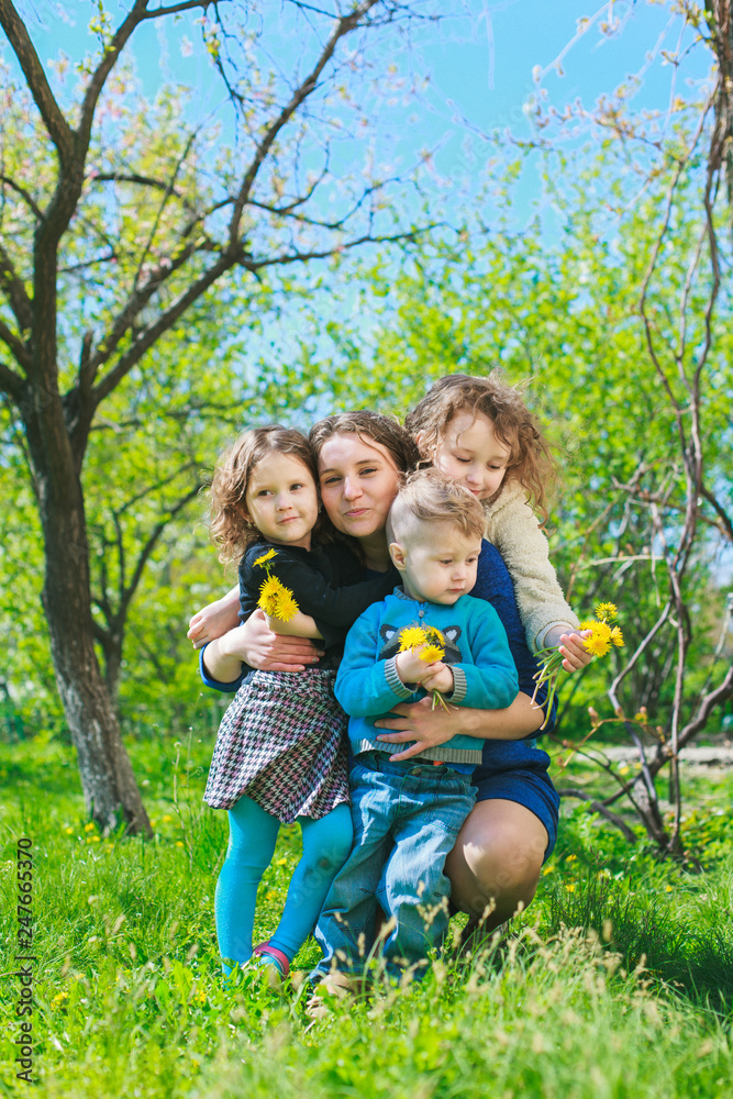 Fototapeta premium Mom with three children - boy and two girls smiling, and her children are hugging. Happy large family in nature.