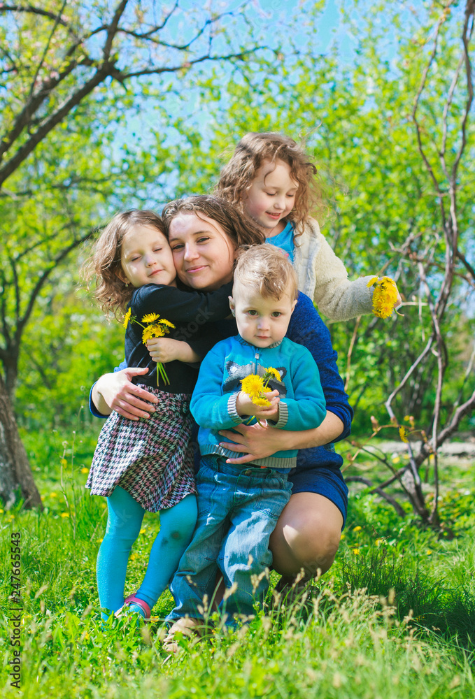 Fototapeta premium Mom with three children - boy and two girls smiling, and her children are hugging. Happy large family in nature.