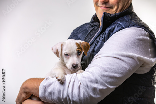 Horizontal portrait of handsome cheerful man holds jack russell terrirer, has glad expression