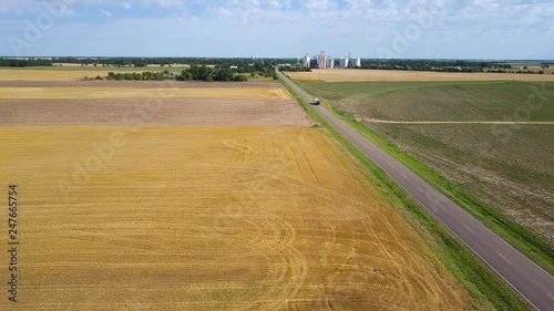 Wide aerial view of country road, RV driving towards farming coop, Kansas, USA
