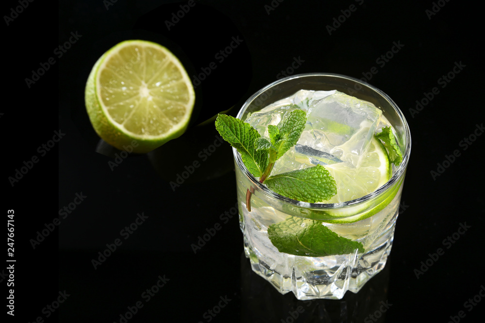 Glass of cocktail with rum, lime, ice cubes and mint leaves on black mirror background. Glass of cocktail with rum, lime, ice cubes and mint leaves on black mirror background.