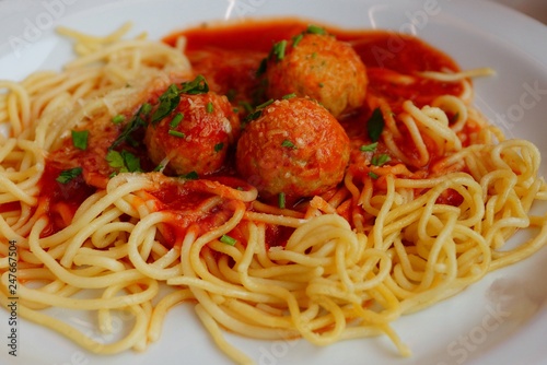 spaghetti with red sauce and round meatballs on a white plate