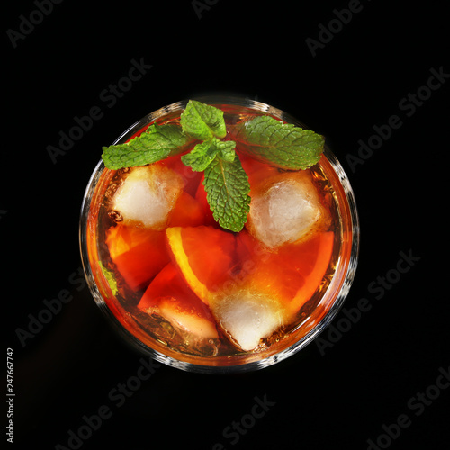 Glass of Dark Rum Cocktail with lime, orange, ice cubes and mint leaves on black mirror background. Top view.