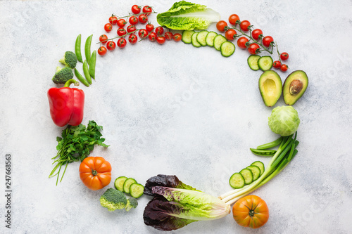 Fresh raw ingredients arranged in a circle frame, tomatoes cucumbers lettuce pepper avocado parsley spring onion broccoli peas on the white table, top view, copy space, selective focus
