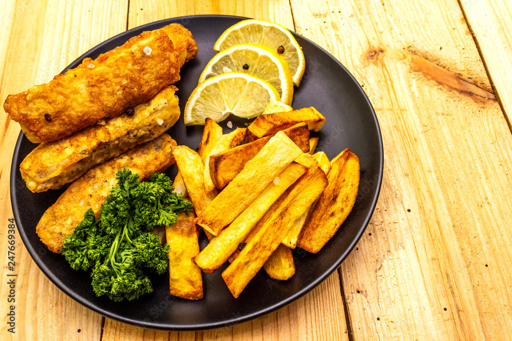 Fish and chips in black plate on wooden table. Traditional British food, close up Fish and chips in black plate on wooden table. Traditional British food, close up