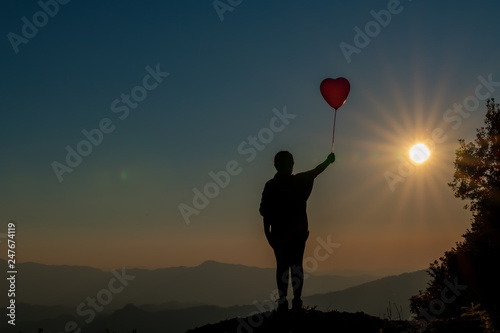 The silhouette of the girl and the balloon on the mountain at sunset