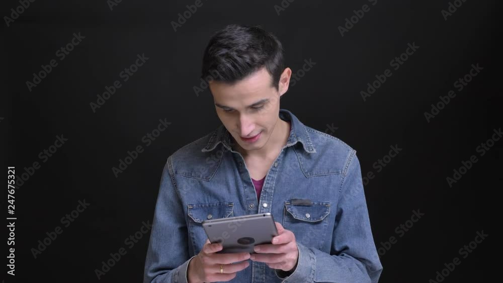 Closeup portrait of young caucasian handsome man browsing on the tablet in front of the camera with background isolated on black