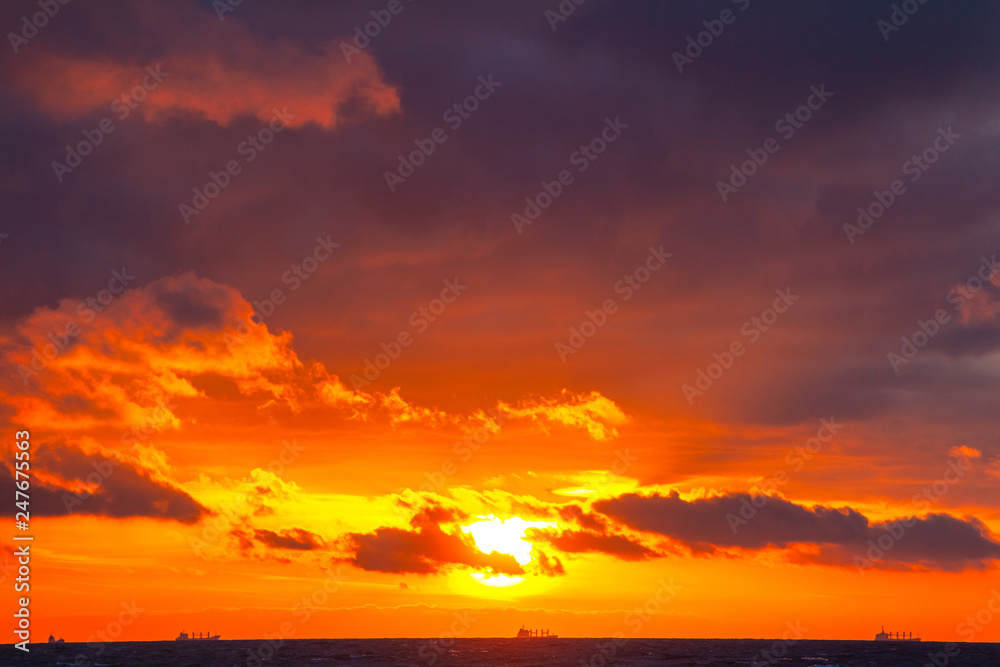 rich bright orange sun in a cloudy sky over the sea during sunset
