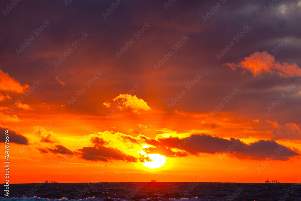 rich bright orange sun in a cloudy sky over the sea during sunset rich bright orange sun in a cloudy sky over the sea during sunset