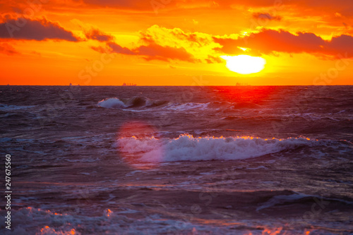 rich bright orange sun in a cloudy sky over the sea during sunset