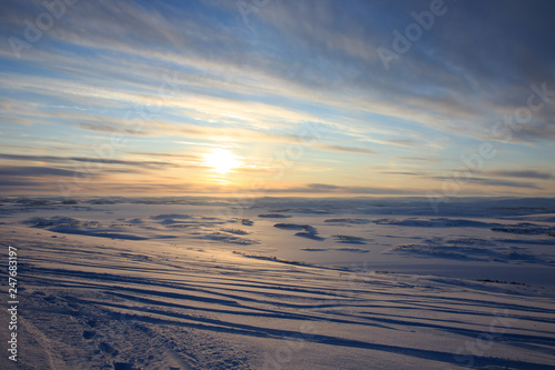 Russian Arctic View  North. Sky with clouds and blue sky reflection in water with waves and snow mountains background with stones grass foreground. Picturesque landscape view  nature scenery beauty