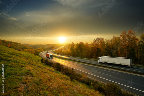 Obraz na płótnie Three trucks driving on the asphalt highway in autumn landscape at sunset w salonie