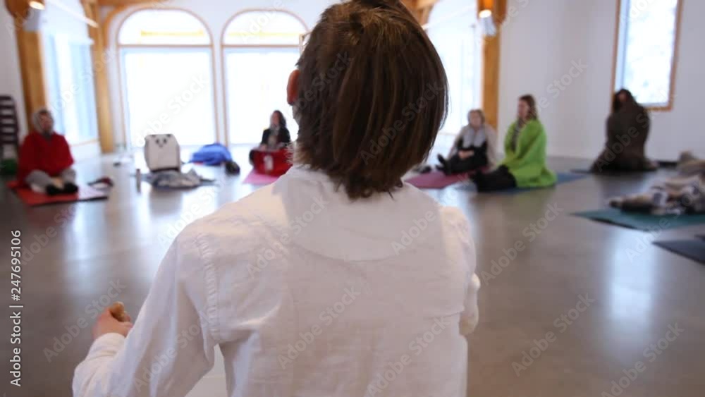 Man performing in front of an audience. Panning right from behind a man dressed in white singing and playing crystal bowls in front of people as part of a healing meditative concert Man performing in front of an audience. Panning right from behind a man dressed in white singing and playing crystal bowls in front of people as part of a healing meditative concert