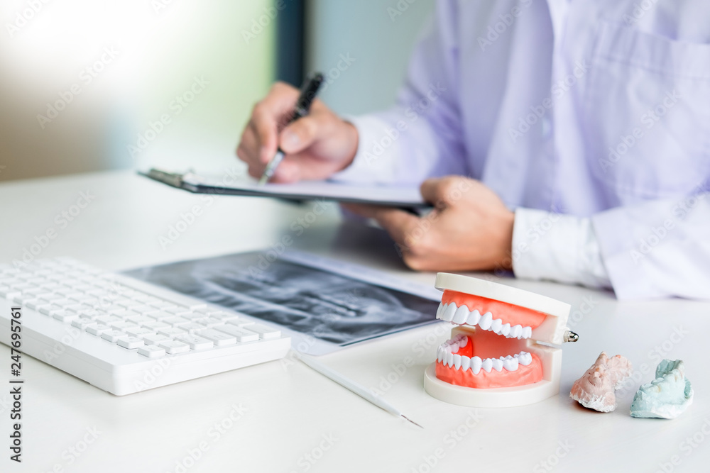 Concentrated dentist sitting at table with jaw samples tooth model in dental office professional dental clinic Concentrated dentist sitting at table with jaw samples tooth model in dental office professional dental clinic