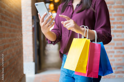 Woman look at mobile phone with paperbags in the mall while enjoying a day shopping.