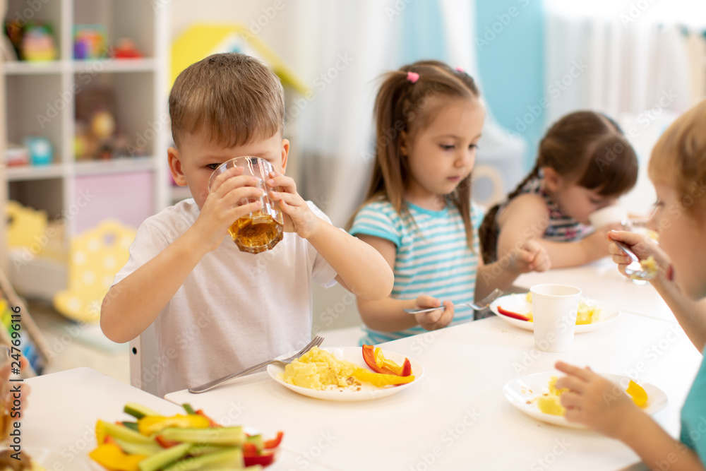Lunch in daycare. Group of children eat healthy food. Kid boy drinking