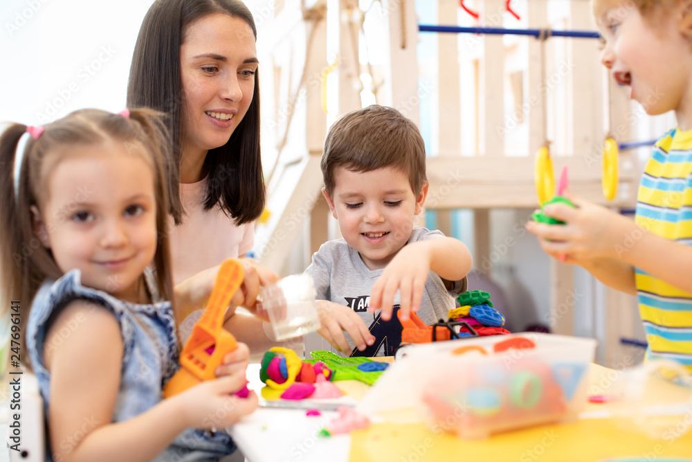 Little children engaged in playdough modeling at daycare. Kindergartener teaches kids molding Little children engaged in playdough modeling at daycare. Kindergartener teaches kids molding