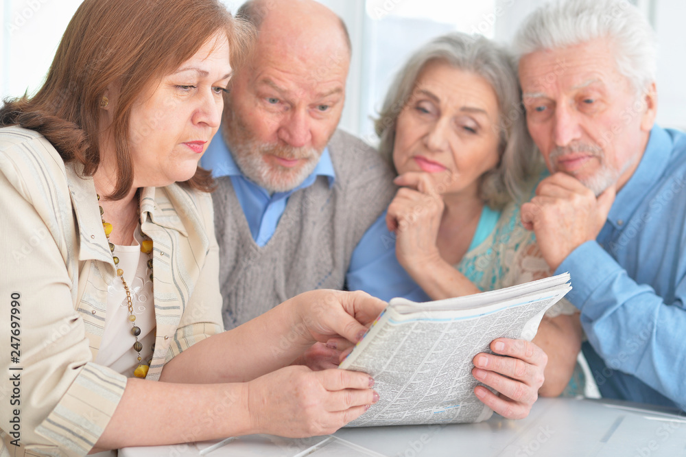 two senior couples sitting at table and reading newspaper