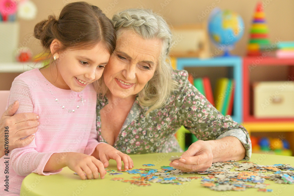 Fototapeta premium Portrait of grandmother collecting puzzle with her granddaughter
