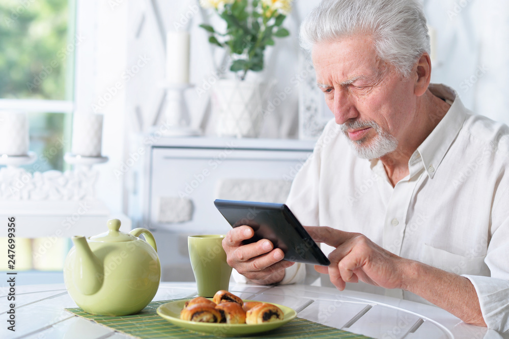 senior man using tablet while drinking tea senior man using tablet while drinking tea
