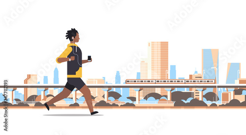 fitness man running outdoor african guy listening to music with headphones on smartphone healthy lifestyle concept cityscape skyscraper background full length flat horizontal