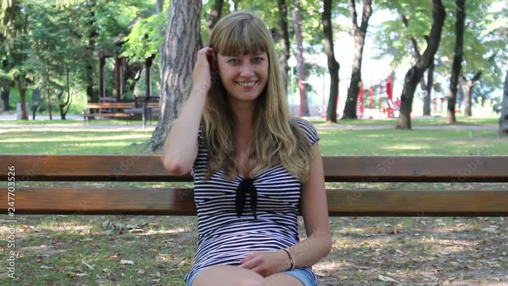 Beautiful Girl is sitting on the bench in a park and smiling Beautiful Girl is sitting on the bench in a park and smiling