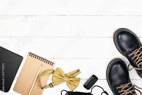 A set of a schoolboy boy: leather shoes, an e-book, a notebook for sketches, pencils, a snack, a banana, a bow tie, headphones in a case, a bag for things, shoes on a light background. Top view. Copy