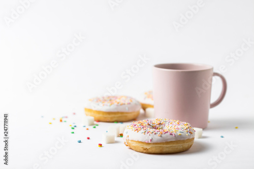 Pink Cup with coffee or tea and fresh tasty donuts, sweet multicolored decorative candy on a white background. Bakery concept, fresh pastries, delicious breakfast, fast food.