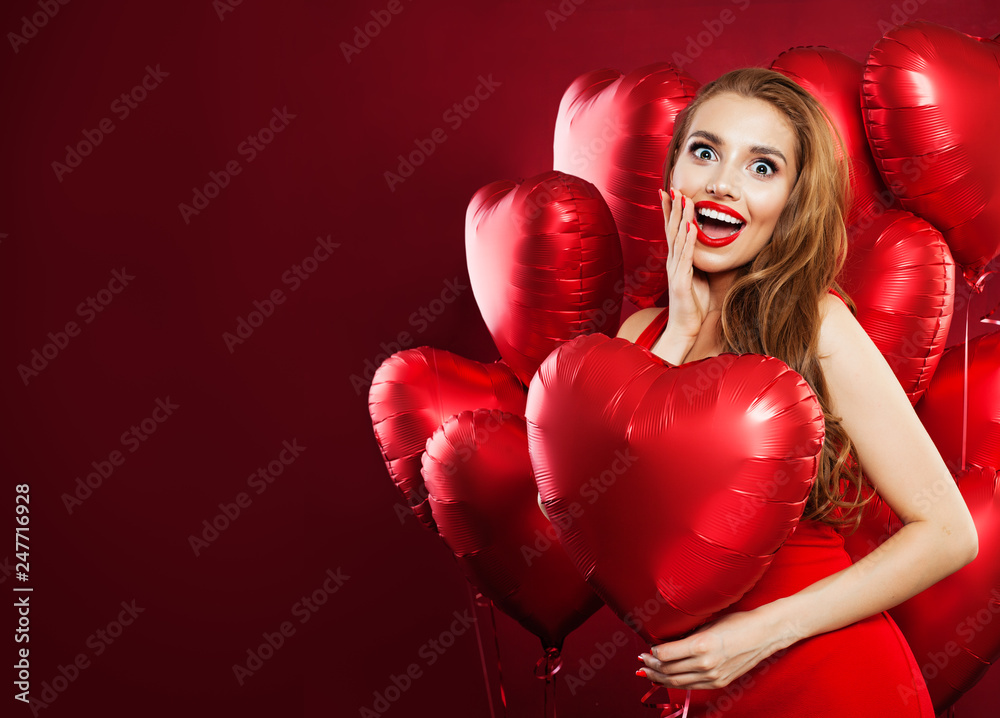 Happy woman in red dress holding balloons red heart on red banner background. Cheerful surprised girl with red lips makeup and cute smile. Surprise, valentines people and Valentine's day concept Happy woman in red dress holding balloons red heart on red banner background. Cheerful surprised girl with red lips makeup and cute smile. Surprise, valentines people and Valentine's day concept