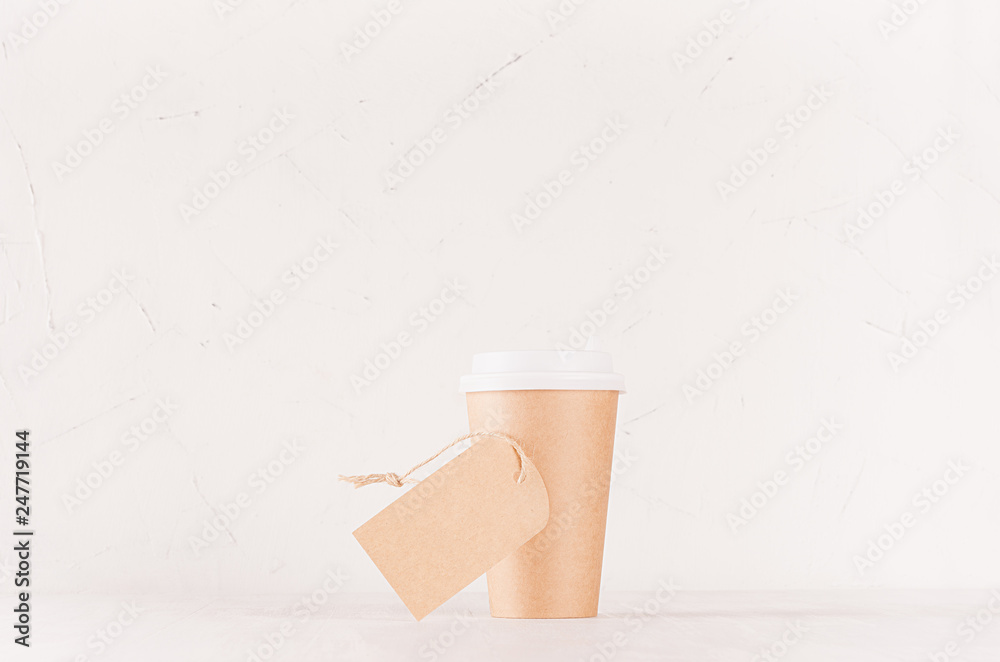 Obraz premium Coffee packing mockup - craft brown paper cup with white cap and blank label on white wood board, coffee shop interior. Modern elegant concept for branding identity, advertising, design.