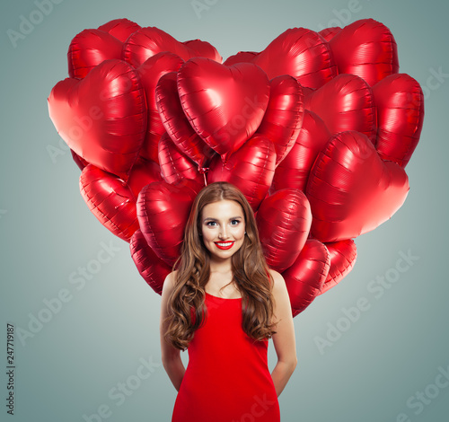 Girl in red dress with heart balloons. Beautiful woman with red lips makeup, perfect curly hair and cute smile. Surprise, valentines people and Valentine's day concept © artmim