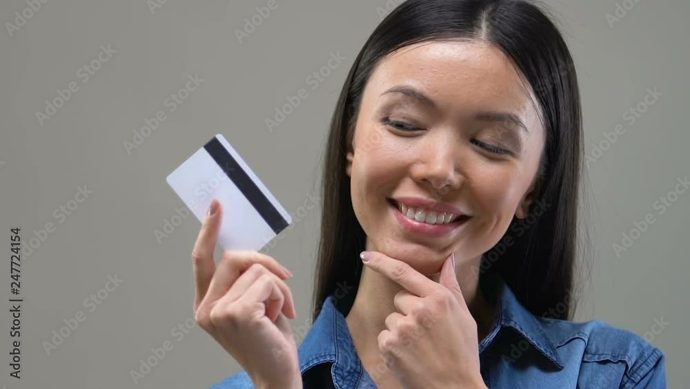 Beautiful Asian woman looking on credit card and thinking about spending money Beautiful Asian woman looking on credit card and thinking about spending money