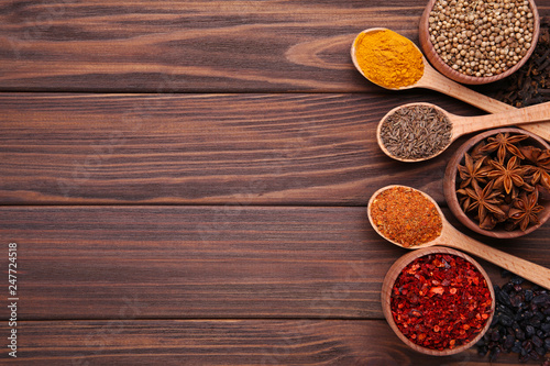 Spices mix on wooden spoons on a brown wooden background. Top view