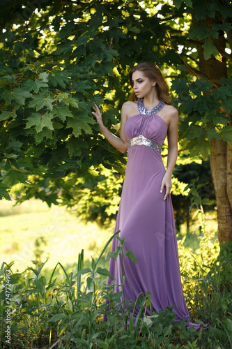 Beautiful slim girl standing in lilac long dress in the park. © ksi