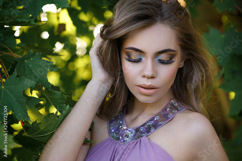Portrait of a beautiful girl in a lilac dress in maple foliage on a summer day.