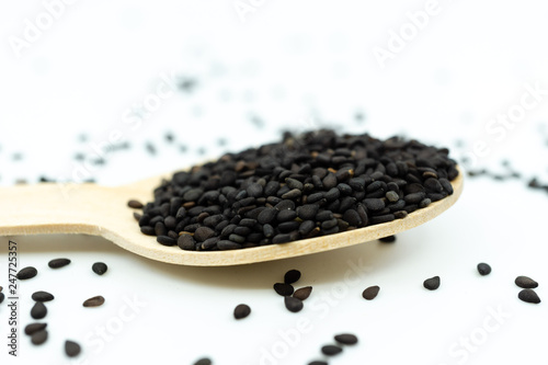 Black sesame on wooden spoon isolated on white background.