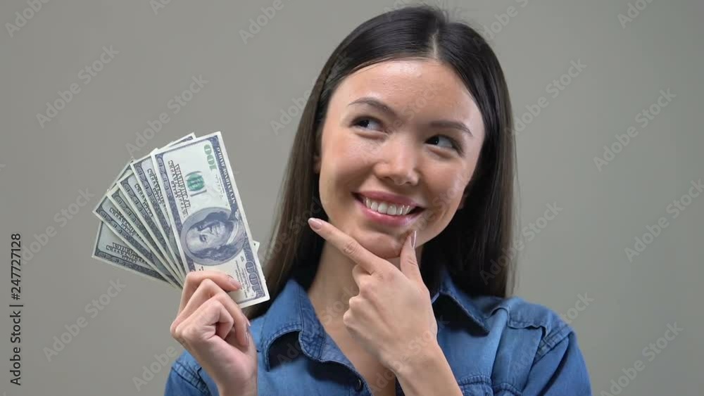 Pensive Asian lady looking at bunch of euros, thinking about shopping, close up Pensive Asian lady looking at bunch of euros, thinking about shopping, close up