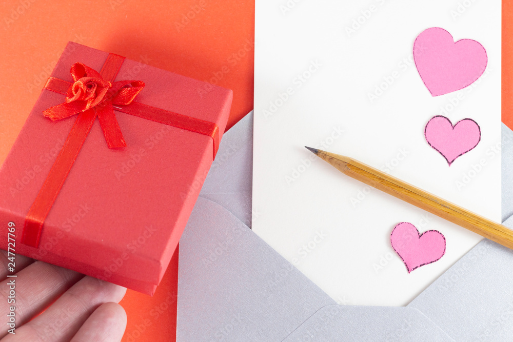 Silver open envelope with white blank letter pink hearts wooden pencil Man hand putting red gift box Red background Empty Space Letter or invitation Minimalist concept Copy Space and template