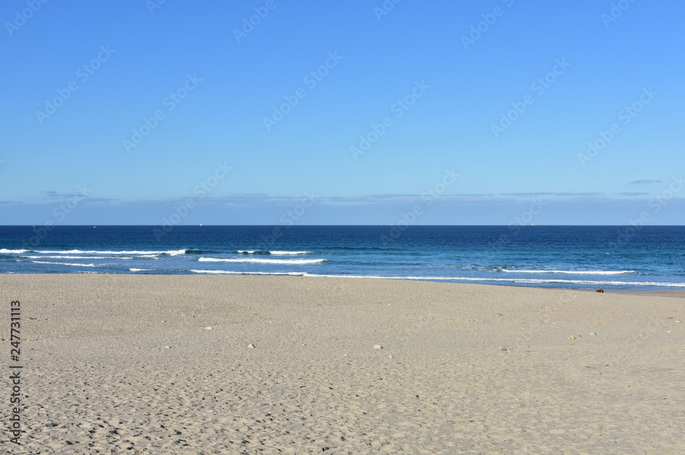 Beach with golden sand and blue sea with small waves with foam. Clear sky, sunny day. Galicia, Spain.