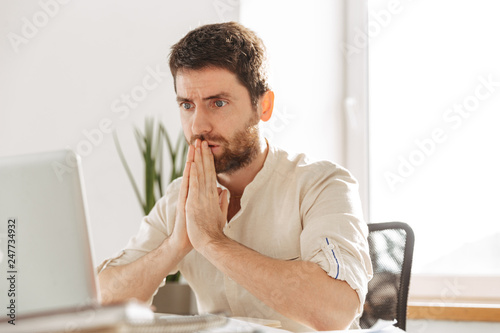 Image closeup of tense businessman 30s wearing white shirt using laptop, while working in modern office