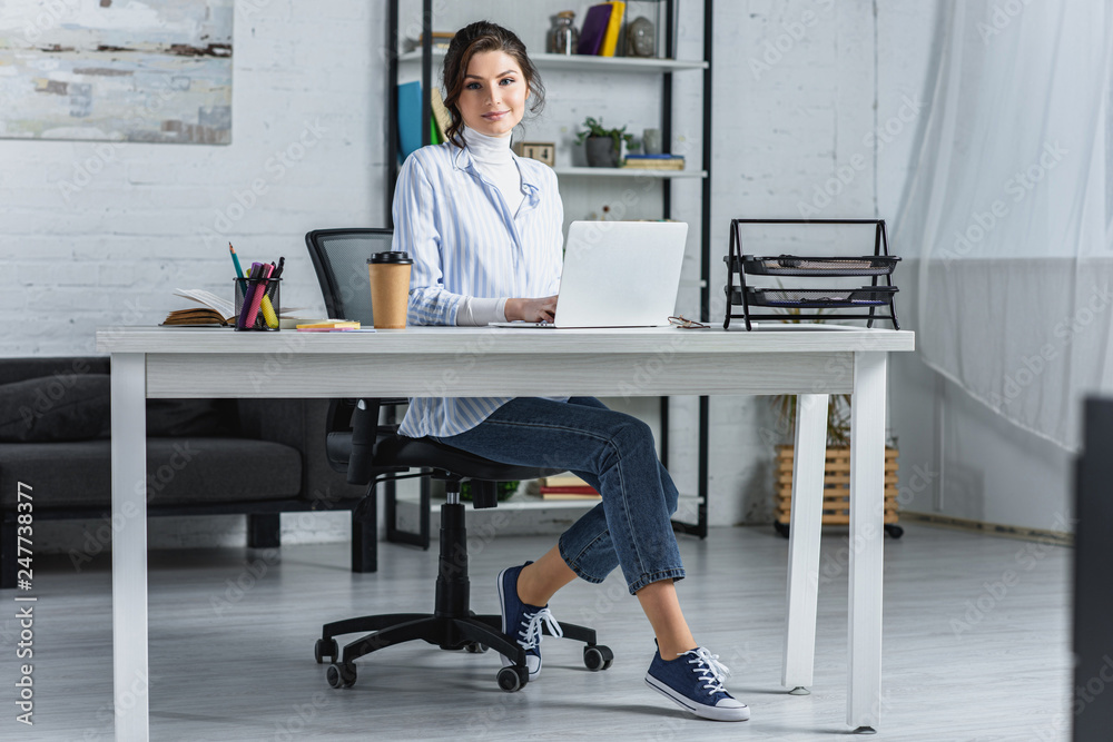 cheerful woman using on laptop while sitting in modern office