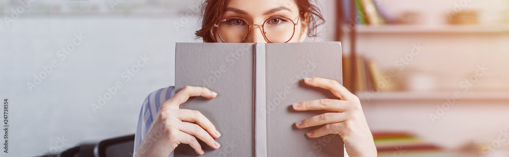 woman in glasses covering face with book - obrazy, fototapety, plakaty 