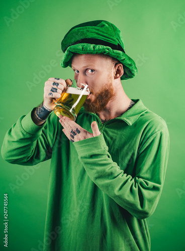 Lucky charms on green background. Leprechauns hat. Man on green background celebrate St Patricks Day. Portrait of excited man holding glass of beer on St Patrick's day isolated on green. photo